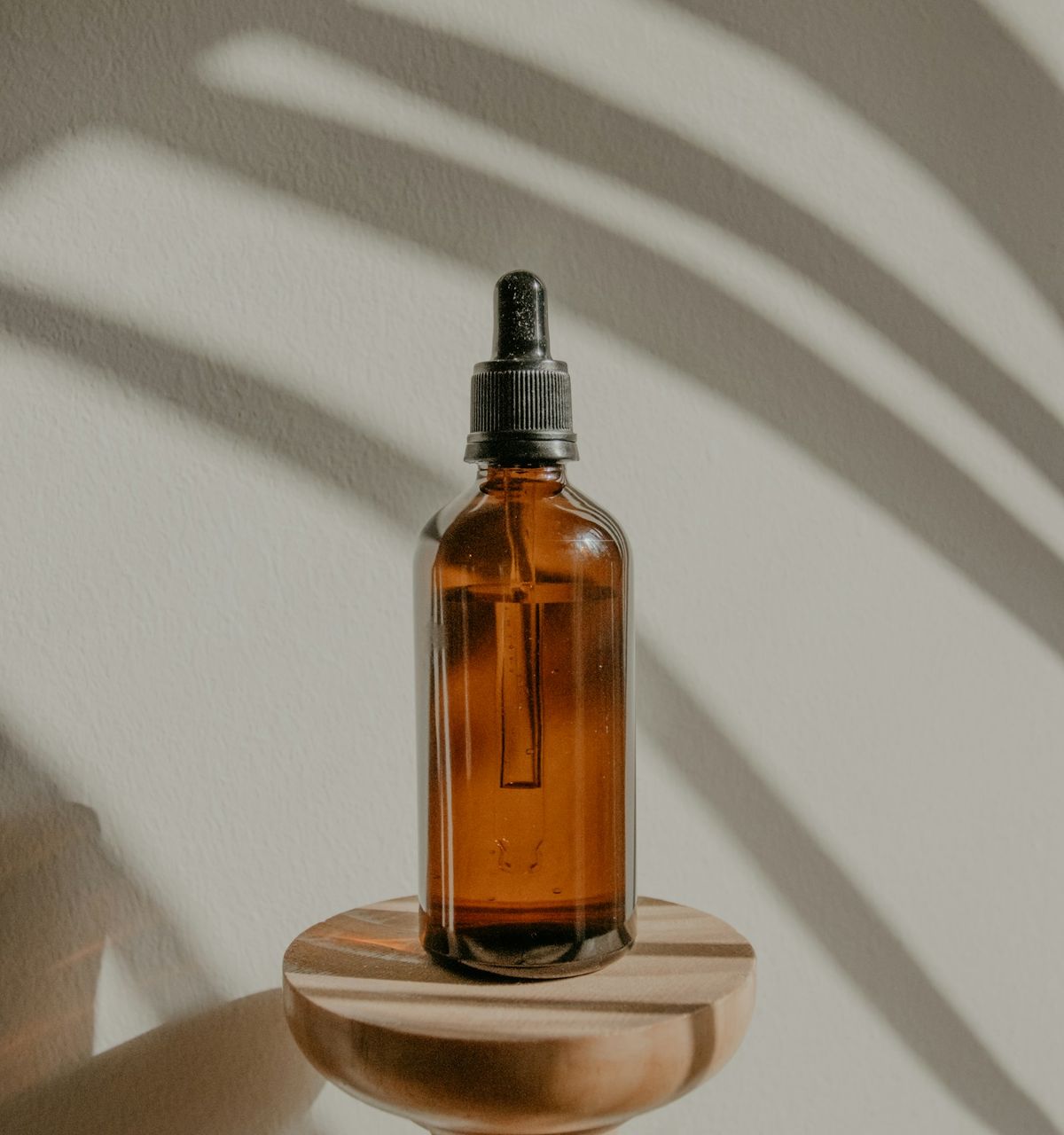 Night Renewal serum in an amber glass dropper bottle on a wooden pedestal, in soft afternoon light.